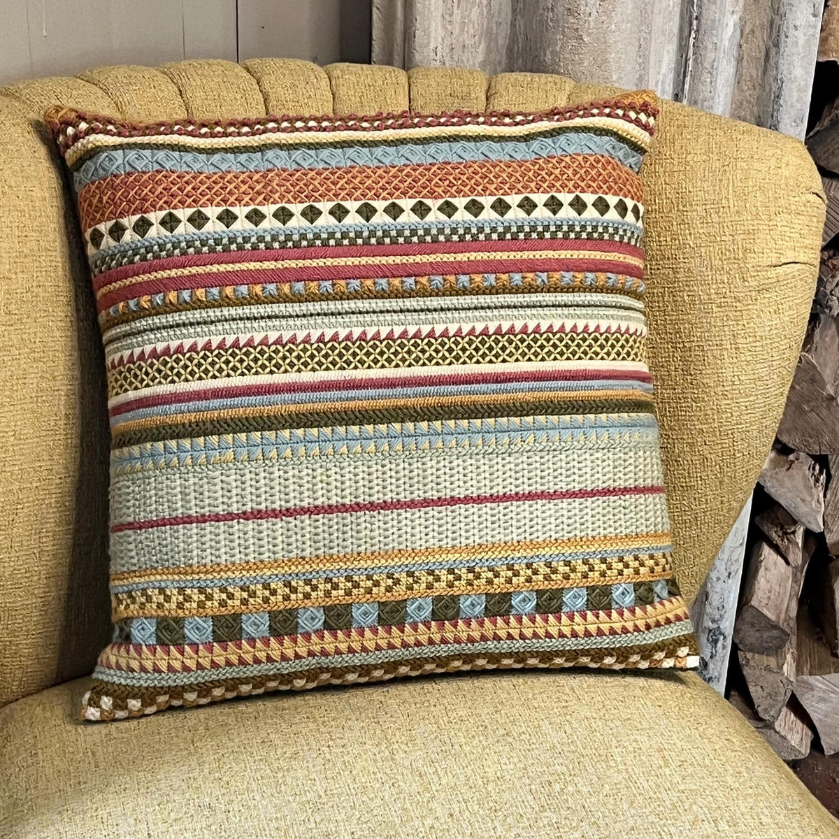 Completed tapestry cushion with multi-coloured striped needlepoint design in terracotta, blue, gold and green, displayed on a yellow armchair