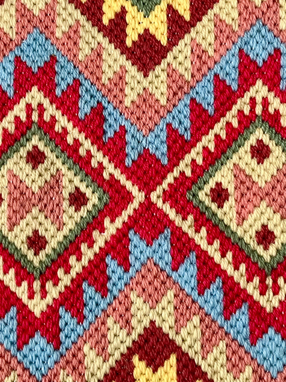 A close-up of a colorful geometric needlepoint fabric pattern with red, cream, light blue, green, and yellow woven details.